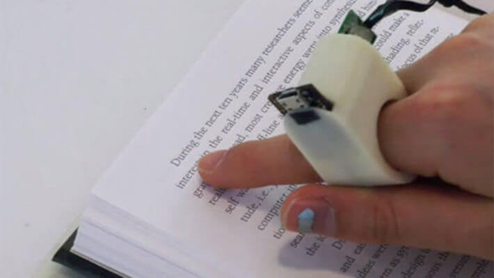 Um dedo, com o anel inteligente, apontando para um texto impresso
